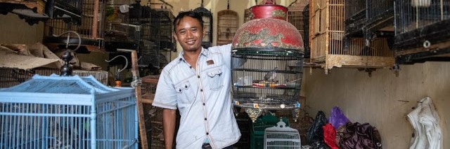 A man holds up a cage with a songbird in it