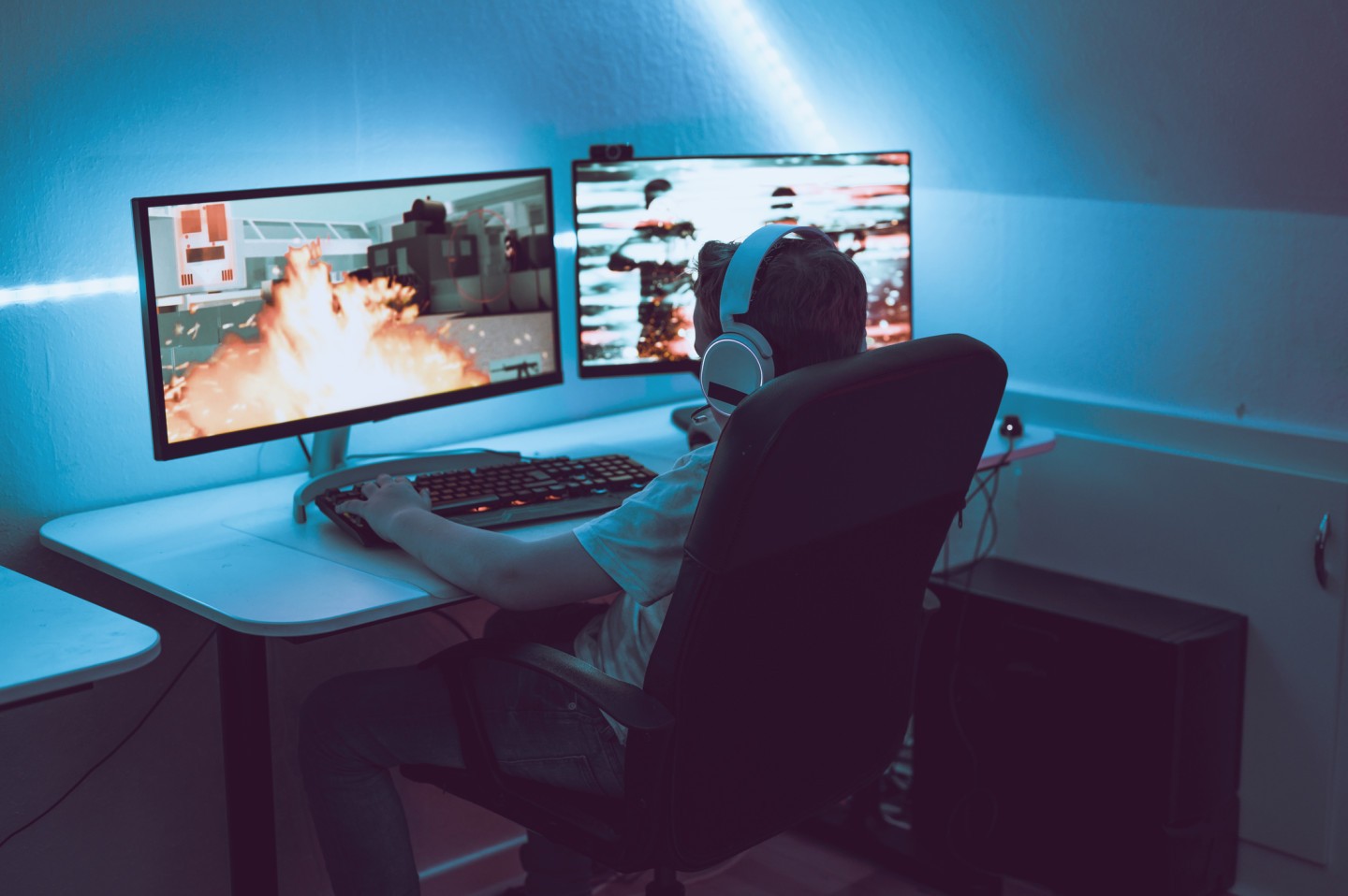 Boy sits in front of two monitors wearing a headset playing an action game