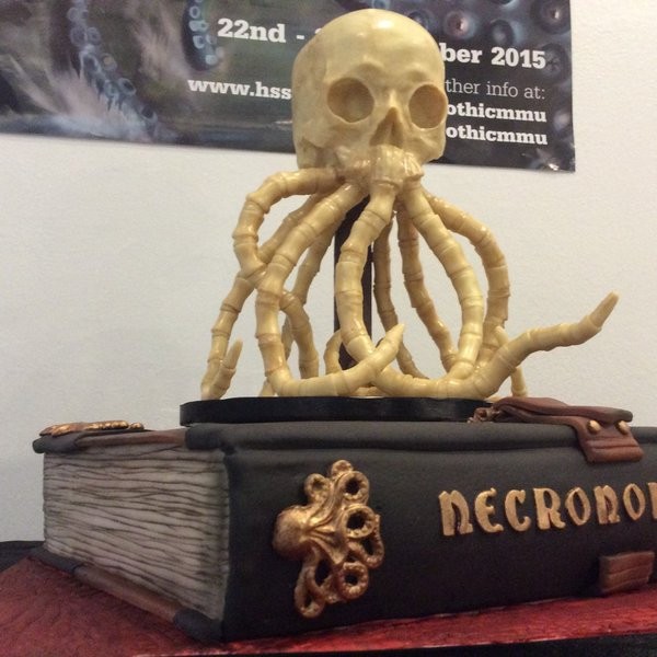 A skull with bony tentacles protuding from its mouth, placed atop a gothic book