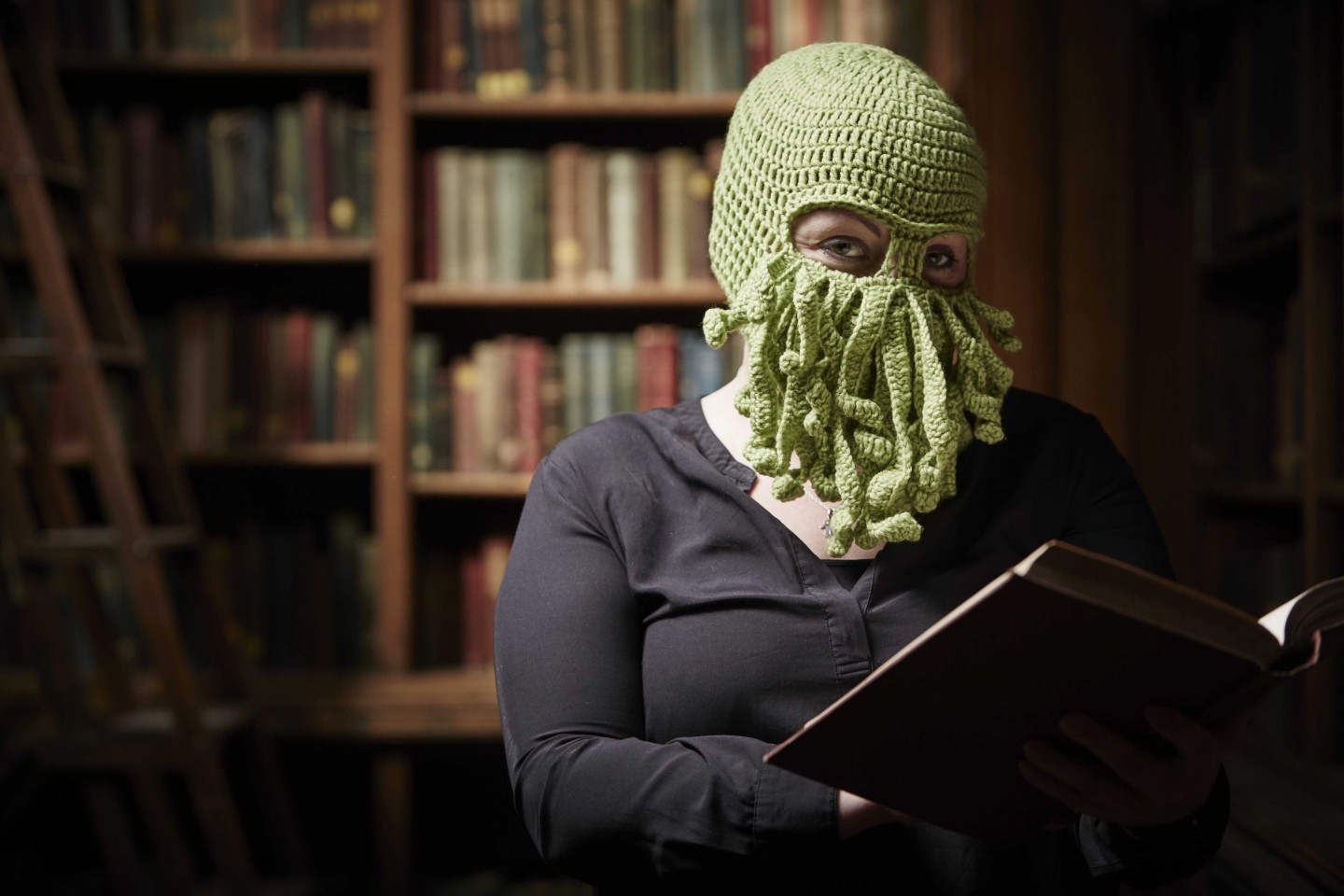 A woman reading in a library wearing a balaclava with tentacles across her mouth