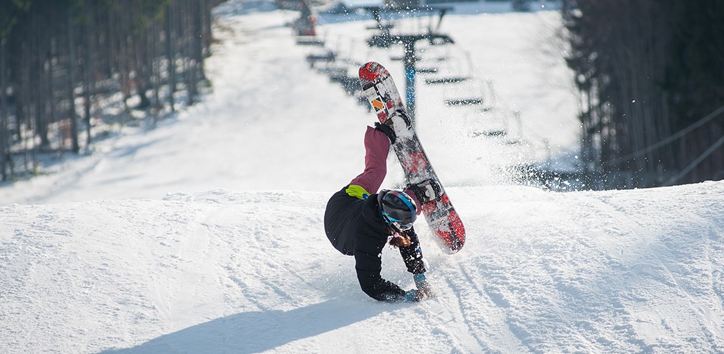 A snowboarder holds out their hands while falling on a ski slope