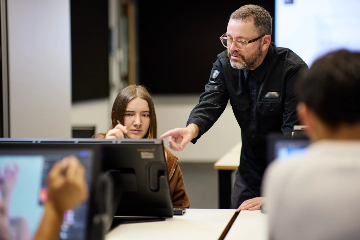 male teacher pointing to a digital screen for female student