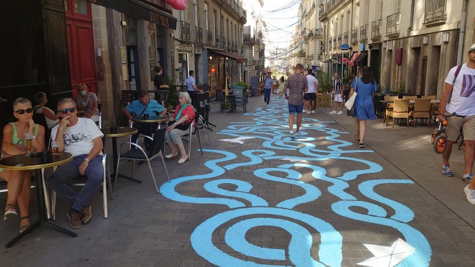 Street with painting on the pavement and people sitting at tables outside cafes