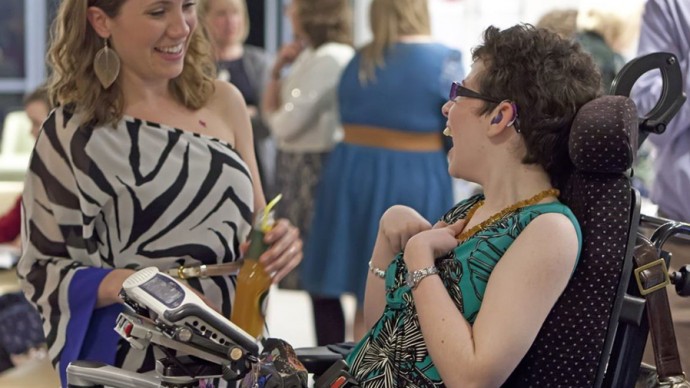 A young person using an assisted communication device laughing with another attendee at an event