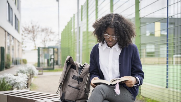 Student reading a book on a bench