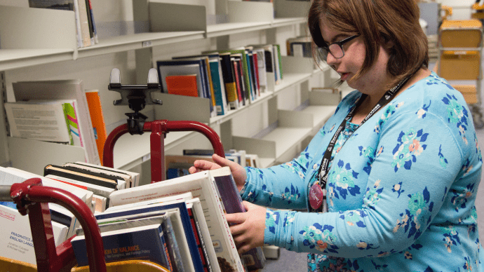 A person with brown hair sorting out books in a library