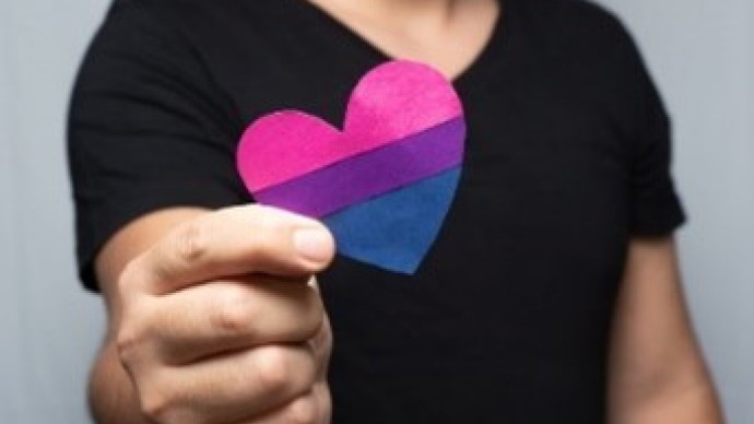 Person holding a heart with bi flag colours: pink, purple & blue