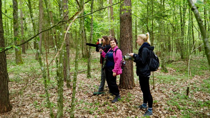 Three students stood in a forest using conservation equipment