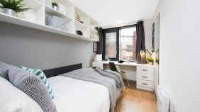 A study bedroom with large bed, shelves, and a desk and chairs