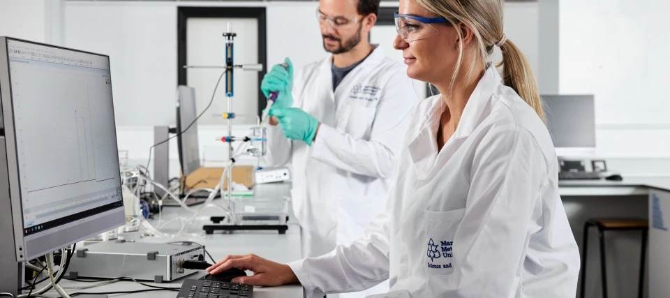 Two students using life sciences laboratory equipment and a computer