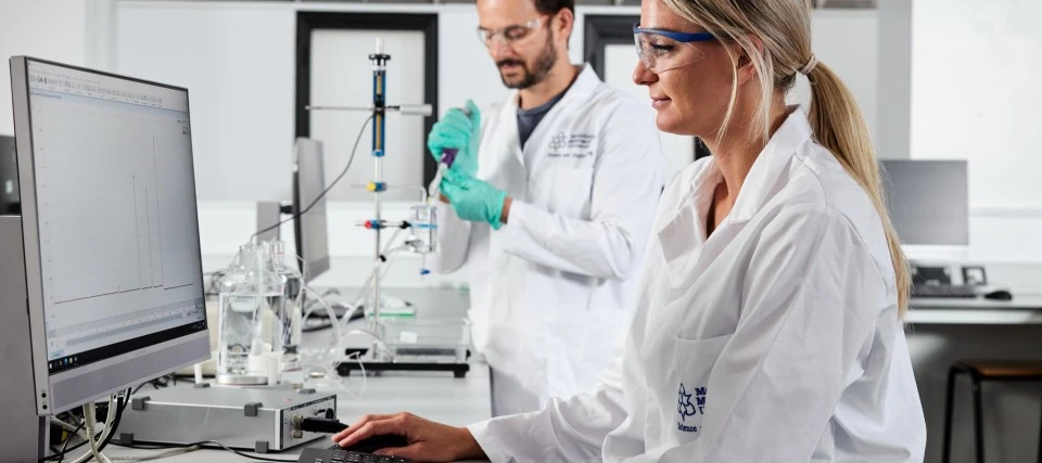 Two student in a lab, one is using a computer and the other is using specialist lab equipment