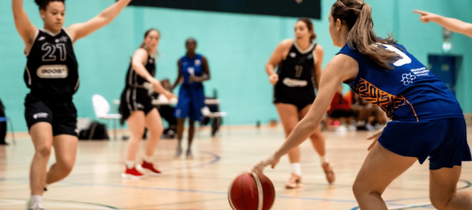 A female netball player on the MMU team being blocked by an opponent.