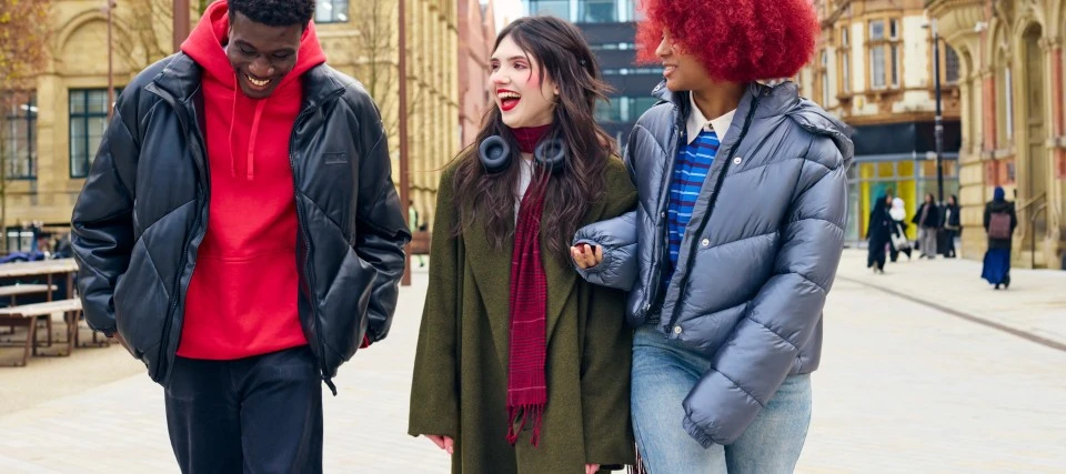 three students wearing bright clothes walking across campus chatting