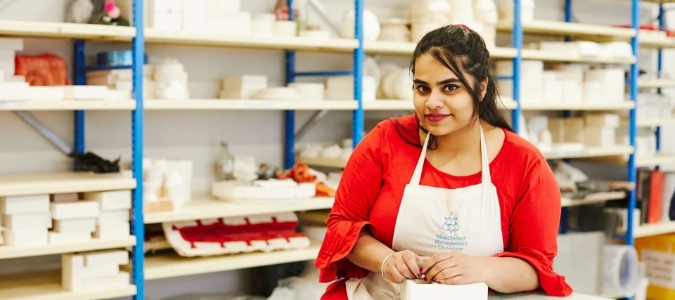 Female art student in a studio sat in front of racking full of ceramics