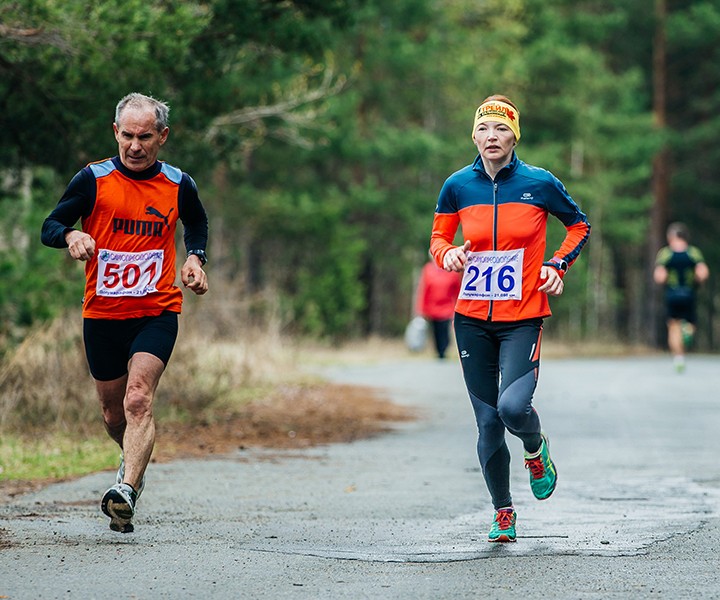 Two masters athletes running down road during a running event in woods