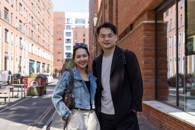 Two students stood outside a University building and smiling.